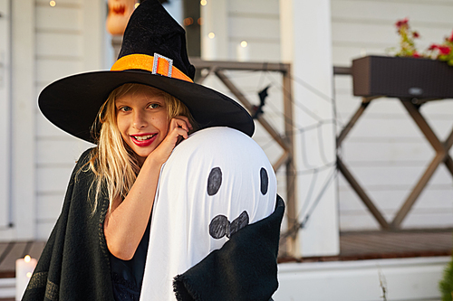 Waist up portrait of cute little girl wearing witch costume  while posing by house on Halloween, copy space