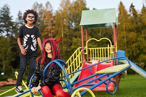 Portrait of two happy littke kids having fun playing on outdoor playground on Haloween, copy space