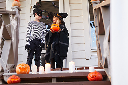 Low angle portrait of two children, boy and girl, standing on porch of decorated house while trick or treating on Halloween, copy space