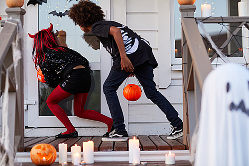 Back view of two kids sneaking by decorated house while trick or treating on Halloween copy space