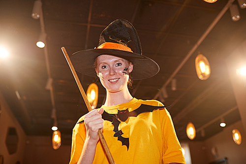 Waist up portrait of adult woman wearing Halloween costume posing as witch and smiling at camera during party, copy space