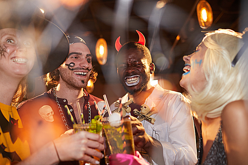 Multi-ethnic group of adult friends wearing Halloween costumes drinking cocktails while enjoying party in club and having fun