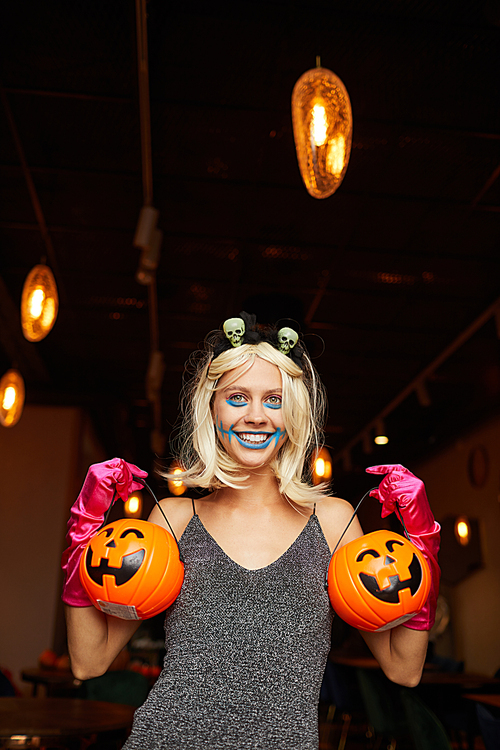 Waist up portrait of fun girl wearing Halloween costume posing with pumpkins during party in night club, copy space