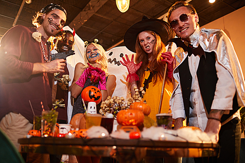Low angle portrait of adult people wearing Halloween costumes posing making faces at camera during party in nightclub, copy space