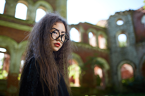 Low angle portrait of little Asian witch posing in abandoned castle on Halloween, copy space