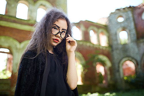 Portrait of teenage Asian girl dressed as witch posing in abandoned castle on Halloween, copy space