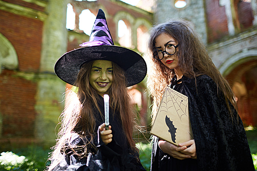 Waist up portrait of two little witches  while posing in abandoned castle on Halloween