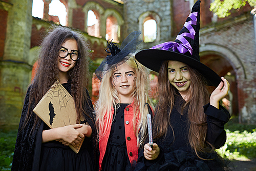 Waist up portrait of three little witches  while posing in spooky castle on Halloween
