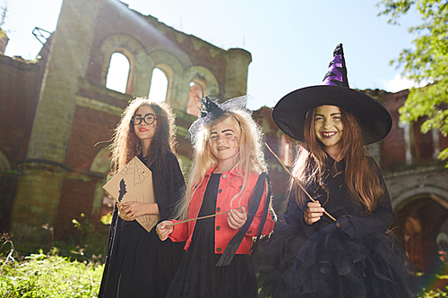 Portrait of three little witches  while posing outdoors on Halloween with spooky castle in background, copy space