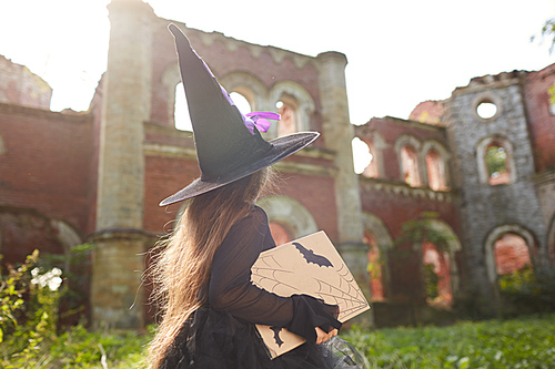 Back view portrait of little witch walking by abandoned castle on Halloween, copy space