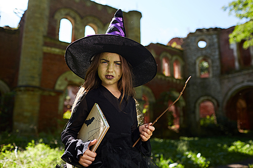 Waist up portrait of little witch posing outdoors on Halloween standing by abandoned castle, copy space