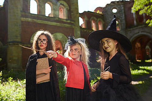 Waist up portrait of three little girls in Halloween costumes posing outdoors in sunlight, copy space