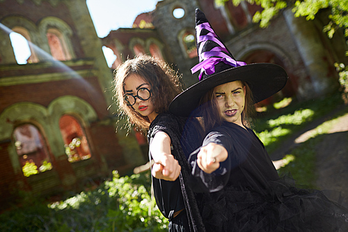 Waist up portrait of two teenage witches posing outdoors on Halloween pointing magic wands at camera, copy space