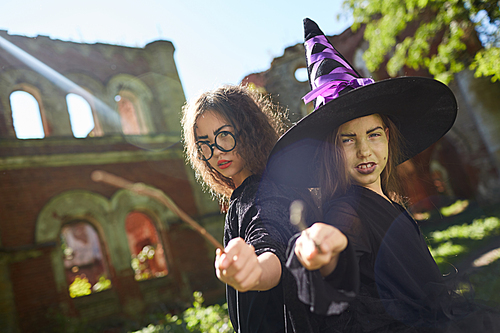 Portrait of two teenage witches posing outdoors on Halloween pointing magic wands at camera, copy space