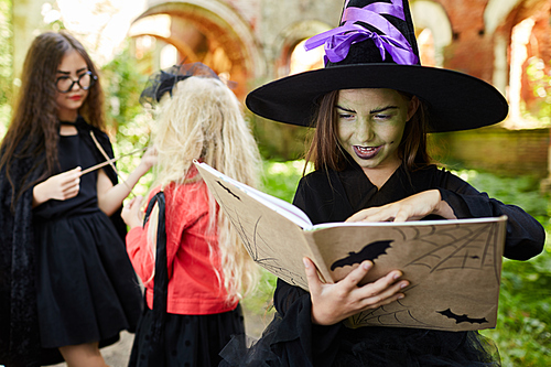 Portrait of children having fun on Halloween focus on little witch holding magic spell book in foreground, copy space