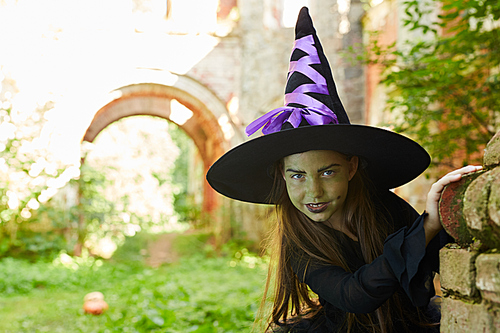 Portrait of little witch  while lurking in castle ruins outdoors, copy space