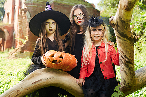 Portrait of three girls wearing Halloween costumes  while posing outdoors with pumpkin