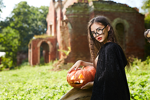 Portrait of teenage Asian girl dressed in Halloween costume posing with pumpkin outdoors, copy space