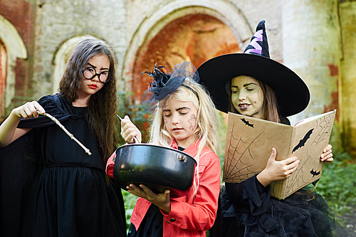 Waist up portrait of three little witches making magic potion on Halloween, copy space