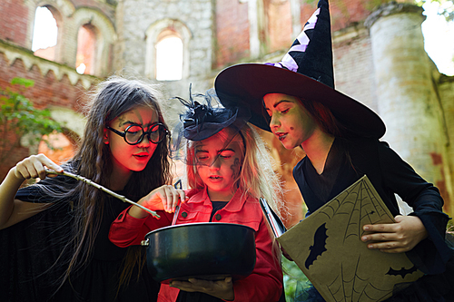 Portrait of three little witches making magic potion on Halloween lit by red light, copy space