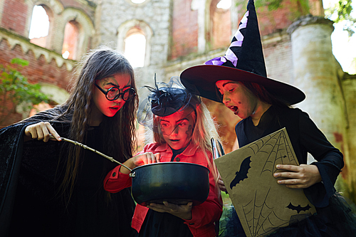 Portrait of three little witches looking in cauldron while making magic potion on Halloween , copy space