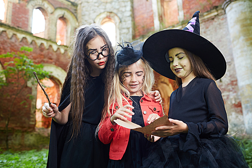Portrait of three little witches reading magic spells outdoors on Halloween , copy space