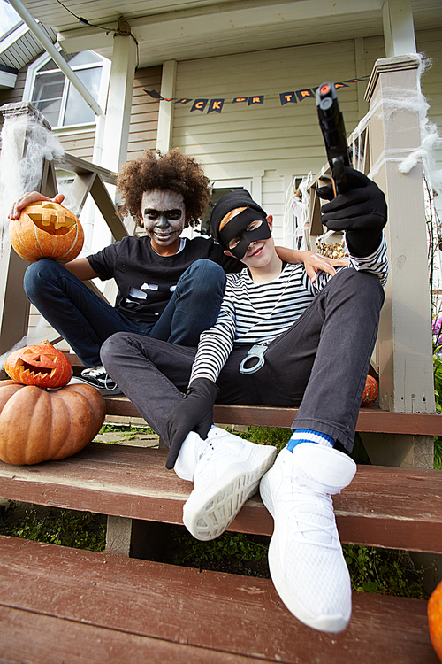 Low angle portrait of two teenage boys wearing Halloween costumes sitting on porch of decorated house and , copy space