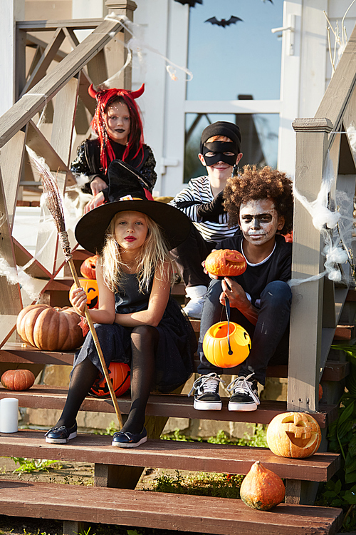 Multi-ethnic group of children wearing Halloween costumes posing on decorated porch while trick or treating together