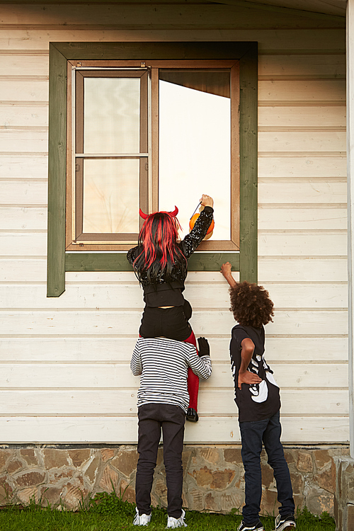 Back view of sneaky kids climbing window of house while trick or treating in Halloween, copy space
