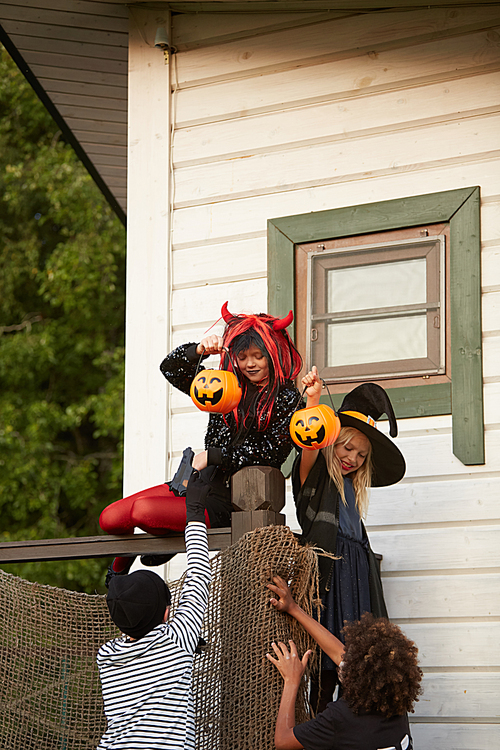 Group of four sneaky kids climbing fence while trick or treating on Halloween, copy space