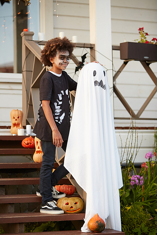 Full length portrait of smiling African-American boy wearing Halloween costume standing on decorated porch while posing outdoors, copy space