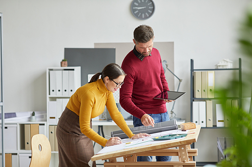 Side view portrait of two architects drawing blueprints while working in office together, copy space