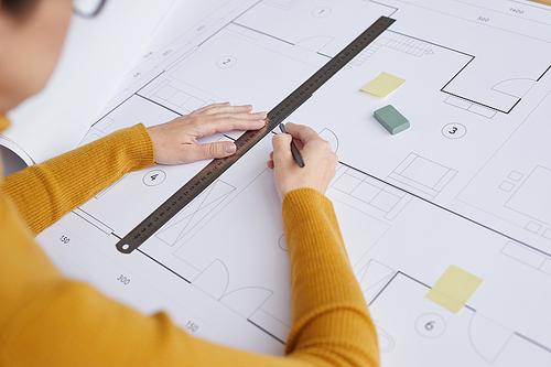 High angle close up of female architect drawing blueprints and plans while sitting at desk in office, copy space