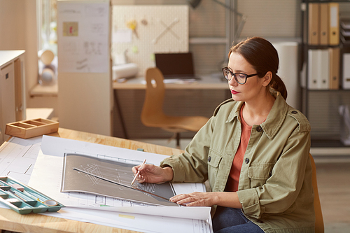 Portrait of young woman drawing blueprints and plans while working at desk in engineers office, copy space