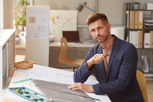 Portrait of mature man drawing blueprints and plans while working at desk in engineers office and , copy space