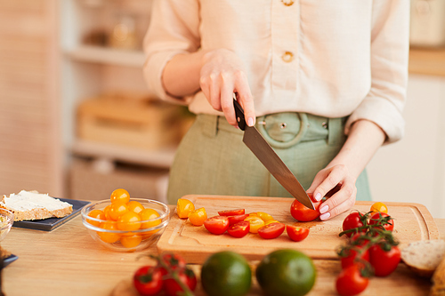 Warm-toned close up of unrecognizable woman cutting fresh tomatoes while cooking healthy breakfast in cozy kitchen interior, copy space