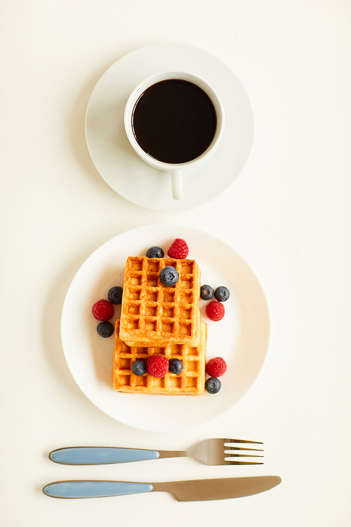 Top view at minimal composition of sweet dessert waffles with berry topping next to single cup of black coffee on white background, copy space