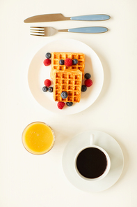 Top view at minimal composition of sweet dessert waffles with berry topping next to cup of black coffee on white background , copy space