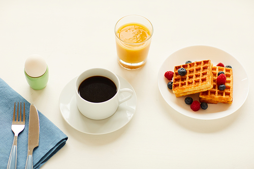 High angle view at delicious gourmet breakfast with sweet dessert waffles, egg and orange juice next to cup of black coffee on white table, copy space
