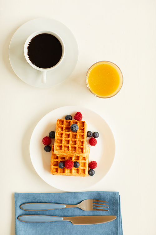 Top view at delicious gourmet breakfast with sweet dessert waffles and orange juice next to cup of black coffee on white table, copy space