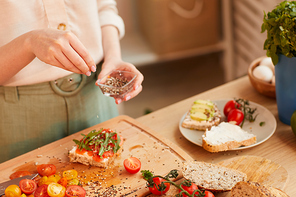 Warm-toned close up of unrecognizable woman preparing healthy breakfast sandwiches with cherry tomatoes and herbs over wholewheat bread, copy space