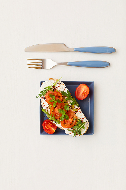 Top view at minimal composition of single bruschetta with cherry tomatoes and herbs next to knife and fork on white background, healthy breakfast and dieting concept, copy space