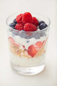 Vertical close up of delicious yogurt parfait cup with fresh berries and granola isolated on white background