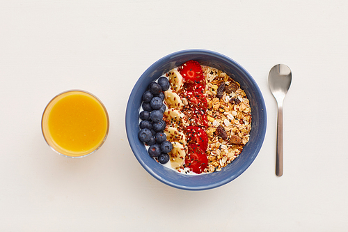 Top view at minimal composition of delicious granola dessert decorated with fruit and berries next to orange juice on white background, healthy breakfast concept, copy space