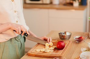 Warm toned closeup of unrecognizable woman cutting fruits while making healthy breakfast in kitchen, copy space