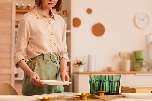 Warm toned mid section portrait of young woman serving table in minimal kitchen interior, copy space