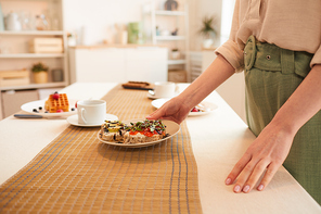 Side view close up of unrecognizable woman putting breakfast plate on dining table in minimal kitchen interior, copy space