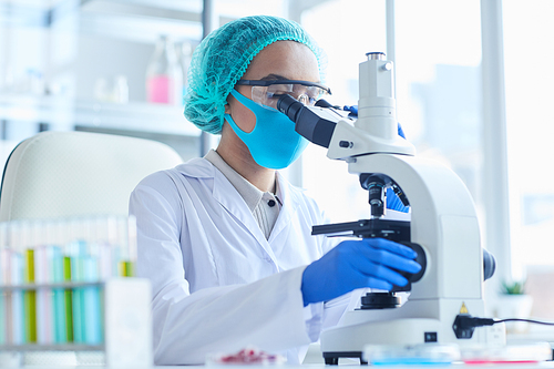 Side view portrait of female scientist looking in microscope while working on research in medical laboratory, copy space