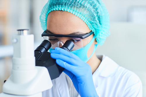 Close up portrait of female scientist looking in microscope while working on research in medical laboratory, copy space