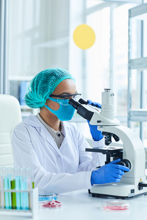 Side view portrait of female scientist looking in microscope while working on research in medical laboratory